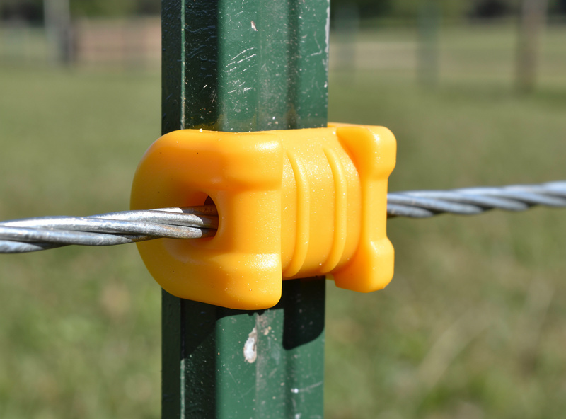 Yellow plastic insulator mounted on a T-post with electric fence wire running through it