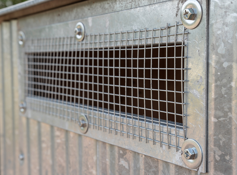 Hardware cloth mesh covering the ventilation opening of a metal chicken coop showing predator-proofing detail