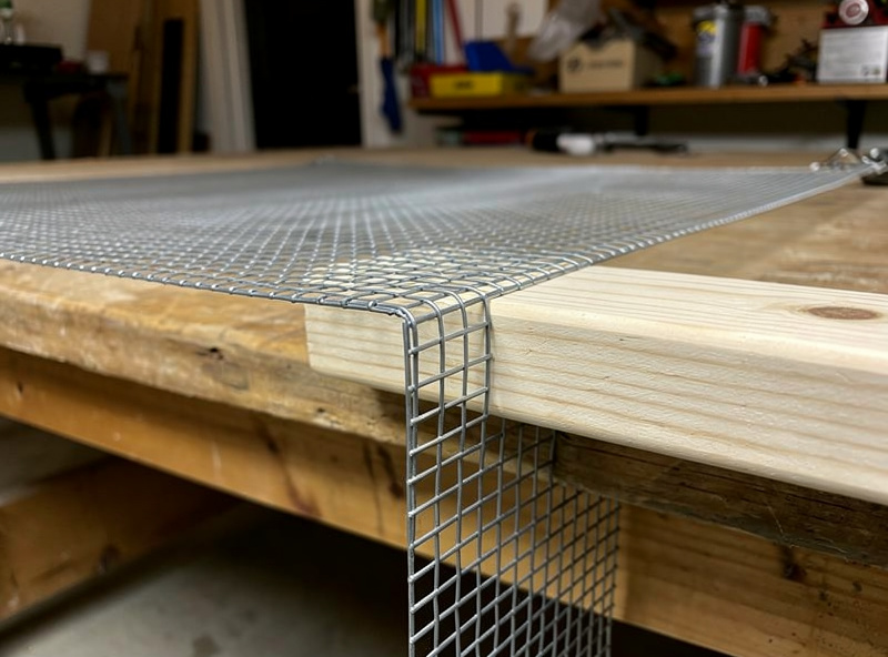 Hardware cloth bent at a sharp 90 degree angle on a workbench using a 2x4 board