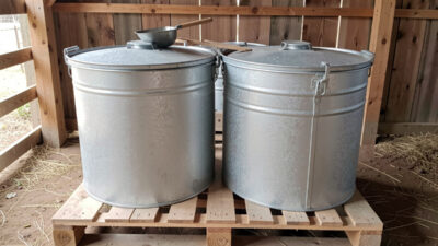 Galvanized steel feed cans with clamped lids storing chicken feed rodent-free in a shed