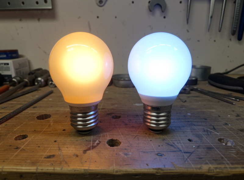 Two LED bulbs side by side, one glowing warm amber and one cool blue-white, for color comparison