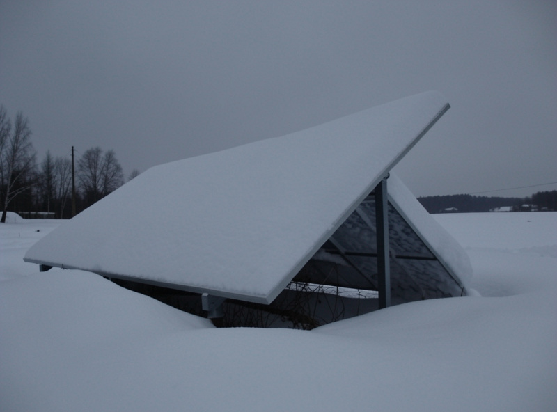 A solar panel completely covered in snow on a grey overcast midwinter day with weak sunlight