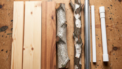 Workbench lineup of roost materials: pine 2x4, hardwood, natural branch, and rejected metal and PVC pipe