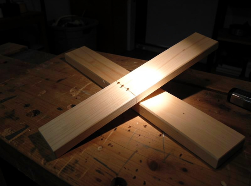 A flat wooden roost bar lifted out and flipped over with a flashlight beam running along the seam to inspect for mites