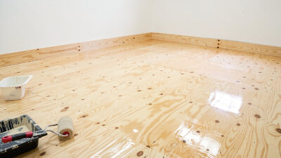 Freshly sealed glossy plywood chicken coop floor drying with roller and paint tray