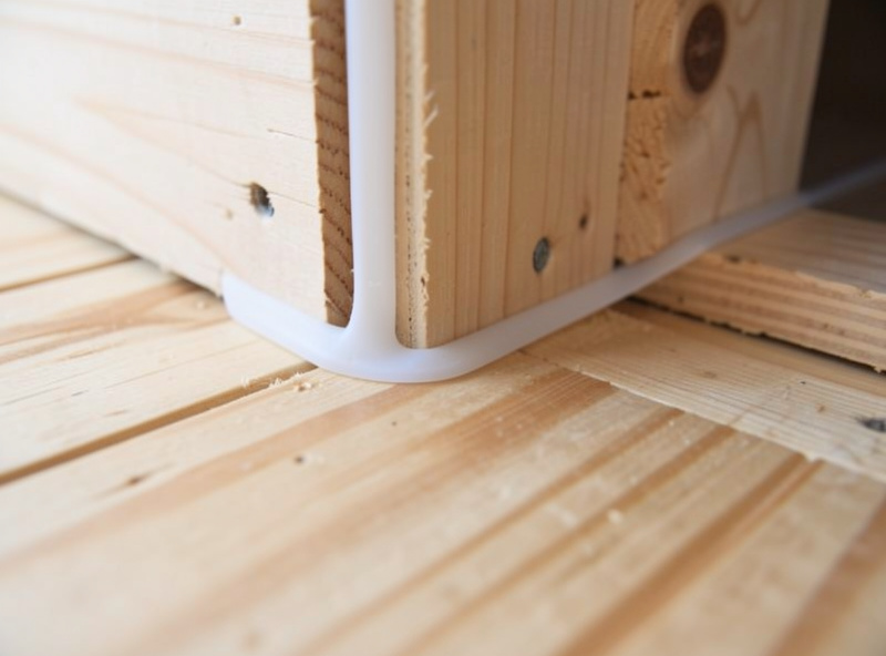 Coved silicone fillet sealing the joint where the plywood floor meets the coop wall